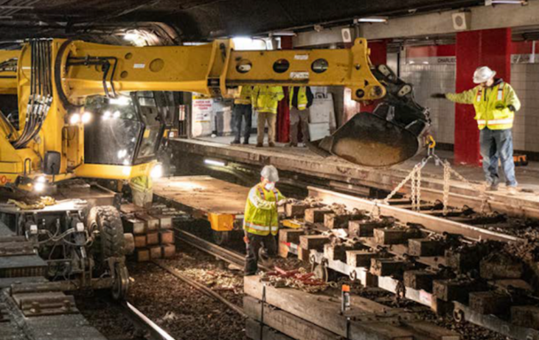 Construction workers use an excavator to move new tracks