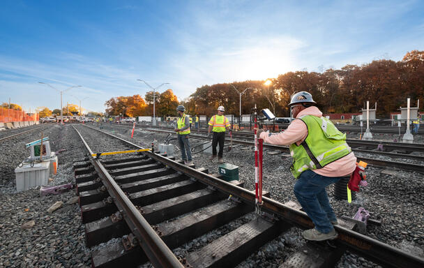 Three construction workers install a new train track on ballast