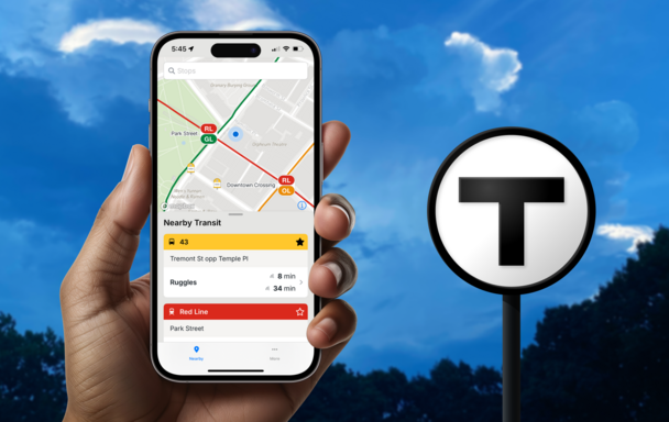 Hand holding an iPhone open to the MBTA Go mobile app, showing live arrival times for nearby Buses and Red Line vehicles.